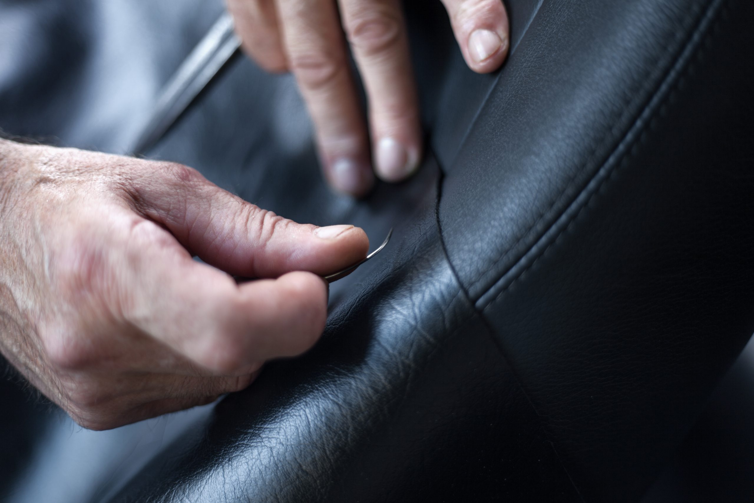 Selective focus shot of a tailor measuring and cutting leather for car seats